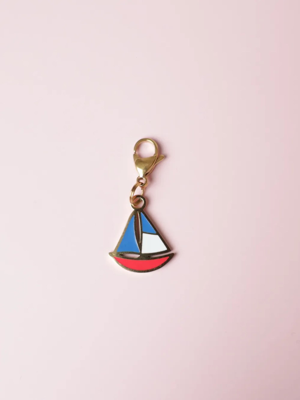 Dog charm in the shape of a golden sailboat with blue and red enamel by Oliva Atelier.Charm para perro en forma de barco velero dorado con esmalte azul y rojo Oliva Atelier.
