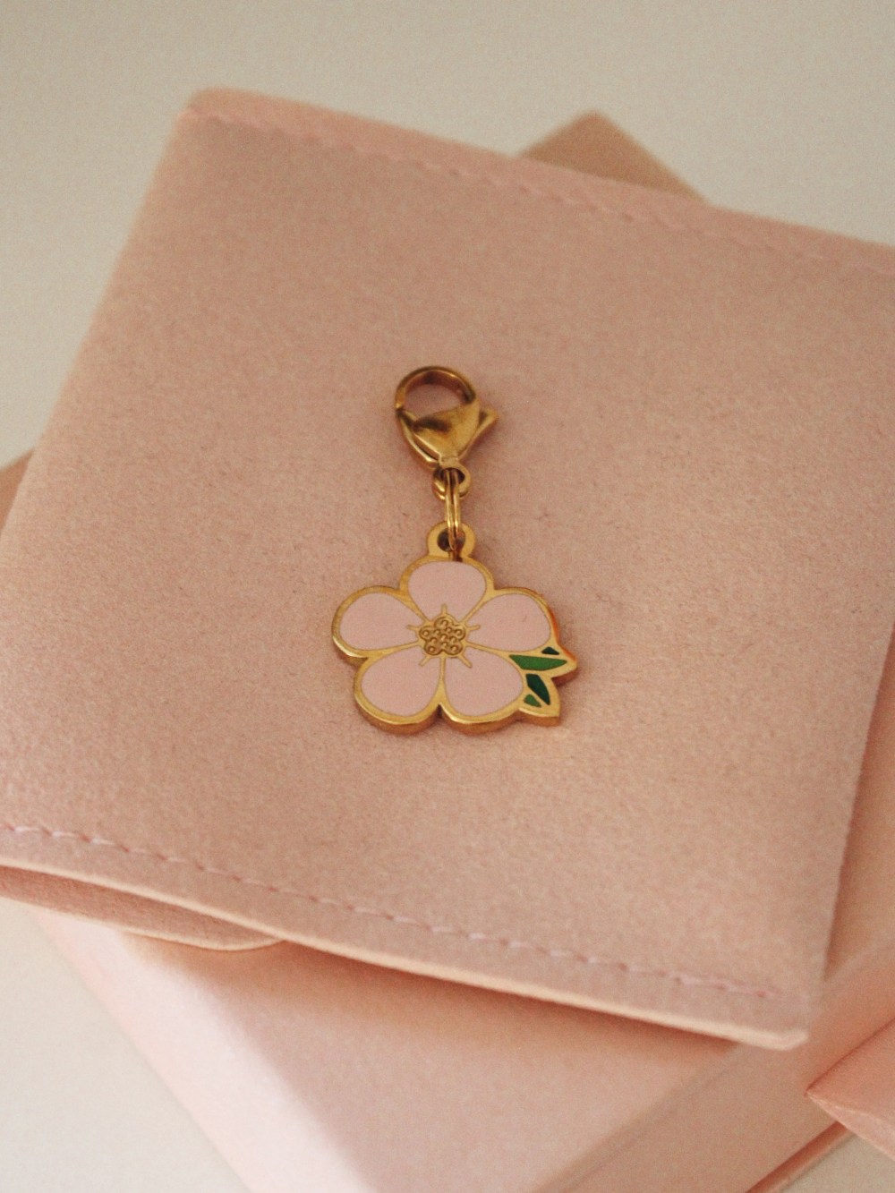 Pink five-petal flower dog charm with green leaves, gold-tone edging and a lobster clasp.