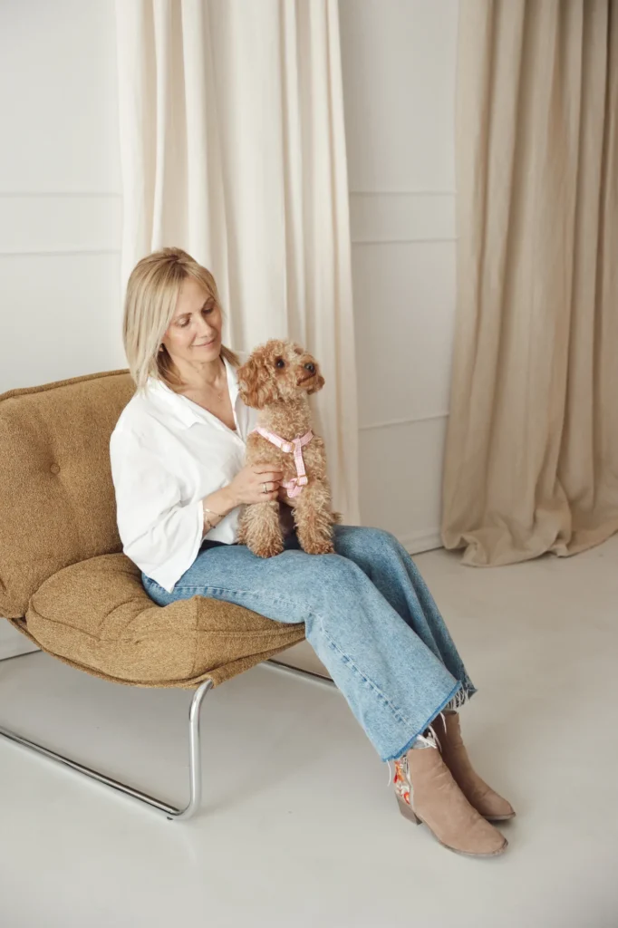 Woman holding a curly-haired dog wearing the pink Vichy harness