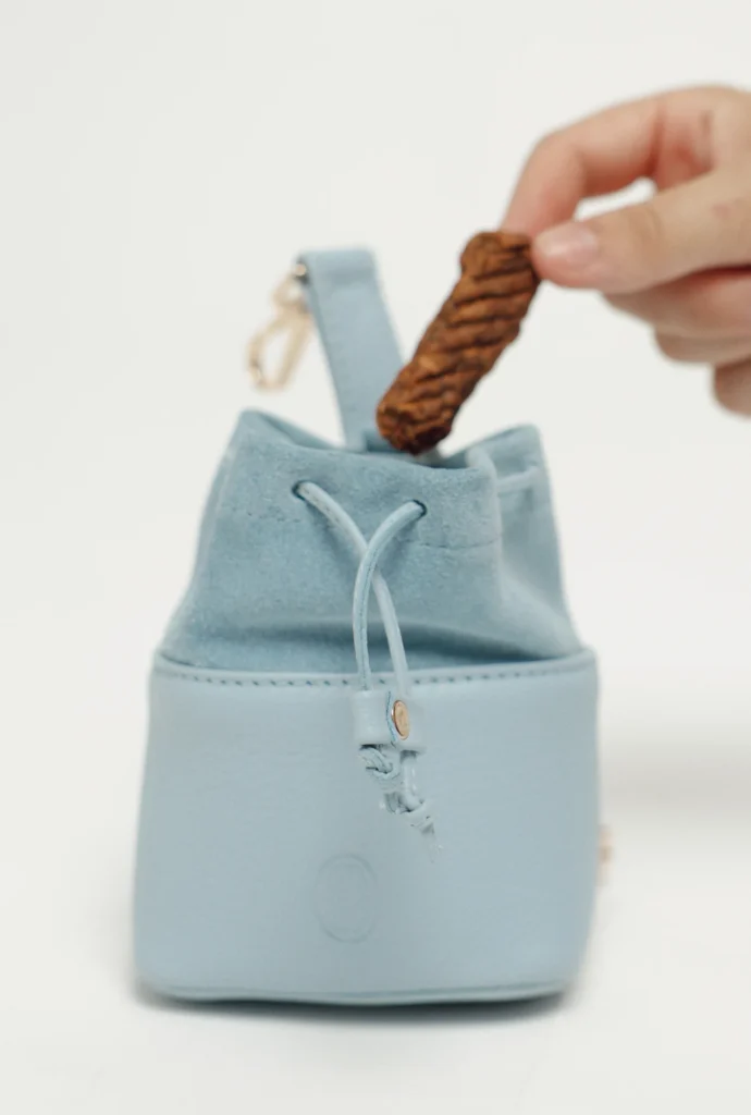 Sky Blue leather treat bag with suede drawstring top and clip, with a treat in hand