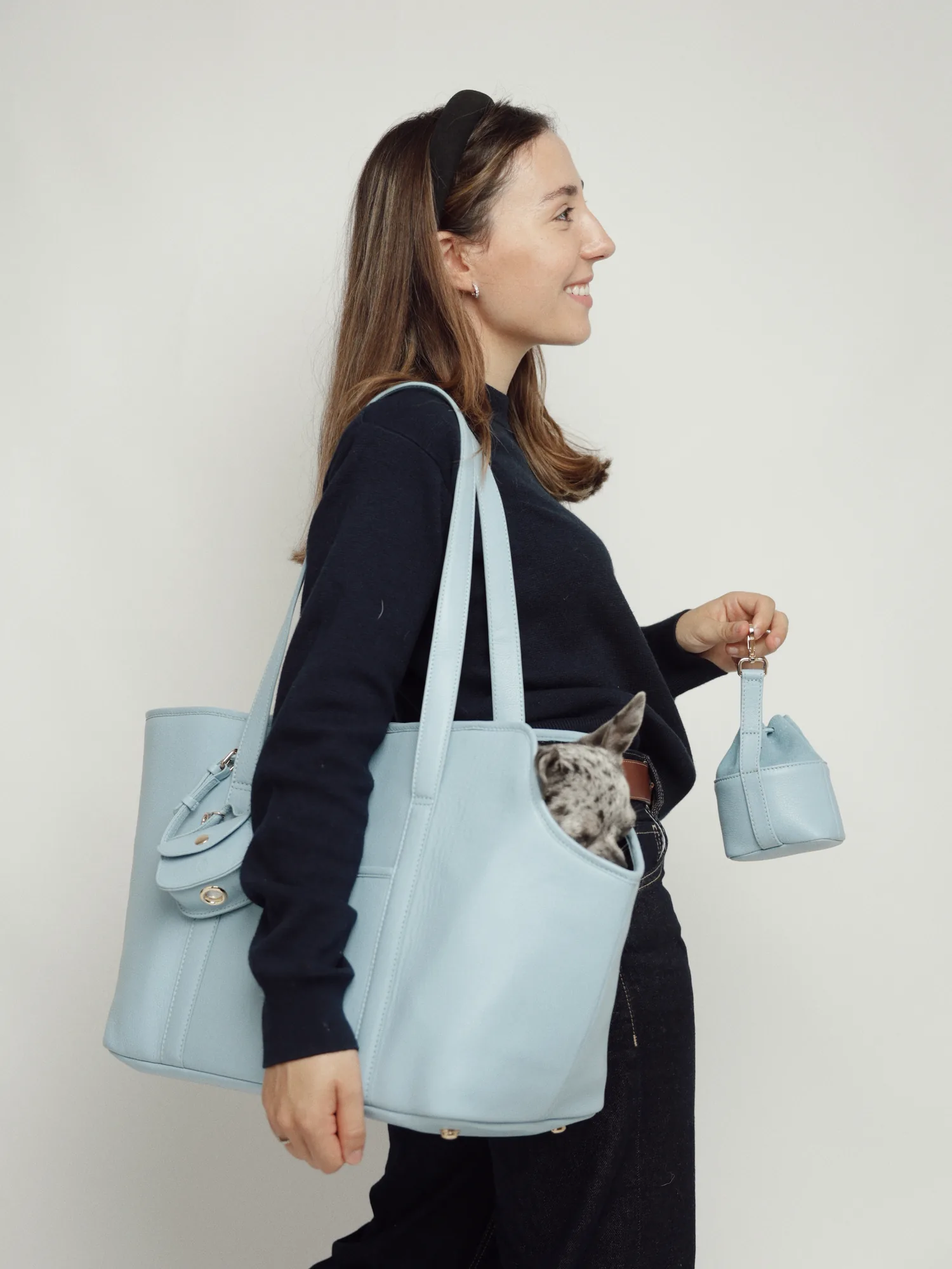 Model carrying the Sky Blue leather dog carrier on the shoulder with a dog inside and the treat bag in hand