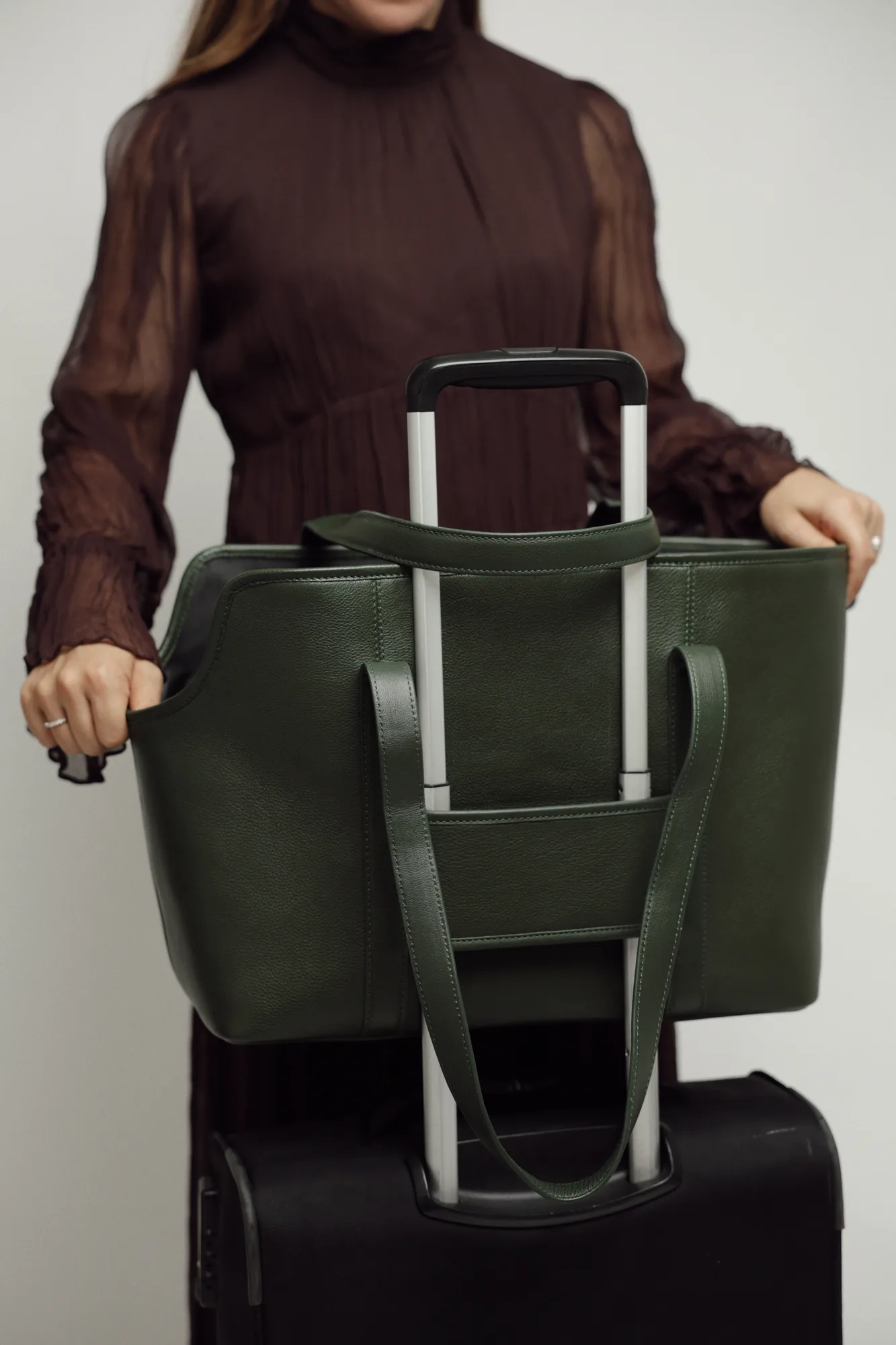 Model holding the Dark Green leather dog carrier slipped over the handle of a wheeled suitcase