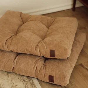 Two beige Atelier dog beds stacked on a wooden floor in a living room