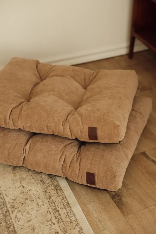 Two beige Atelier dog beds stacked on a wooden floor in a living room