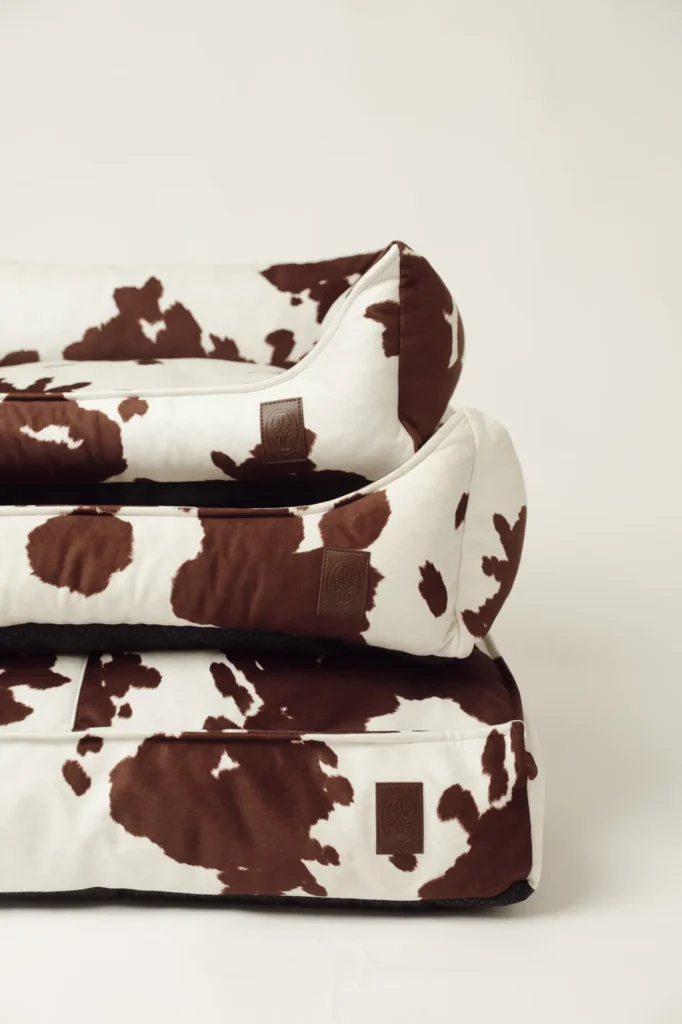 Close-up of stacked Moo cow print dog beds with leather Oliva logos