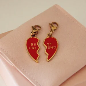 Pareja de charms Best Friends de corazón partido rojo con mosquetones dorados sobre una funda rosa palo
