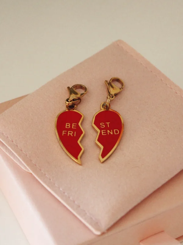 Pair of red split-heart Best Friends charms with gold-tone clasps on a pale pink pouch