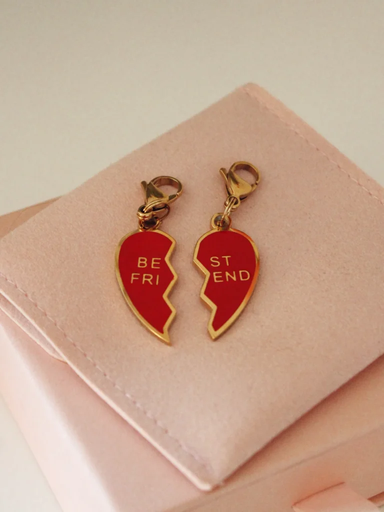 Pareja de charms Best Friends de corazón partido rojo con mosquetones dorados sobre una funda rosa palo