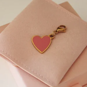 Pink enamel heart charm with a gold-tone border and clasp on a pale pink pouch