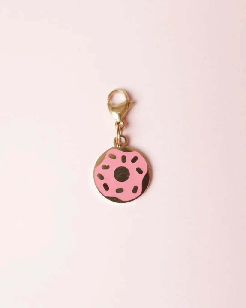 Pink-frosted donut charm with sprinkles and a gold-tone clasp on a pale pink background