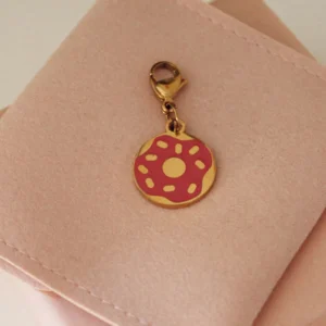 Charm de dónut con glaseado rosa y virutas y mosquetón dorado sobre una funda rosa palo
