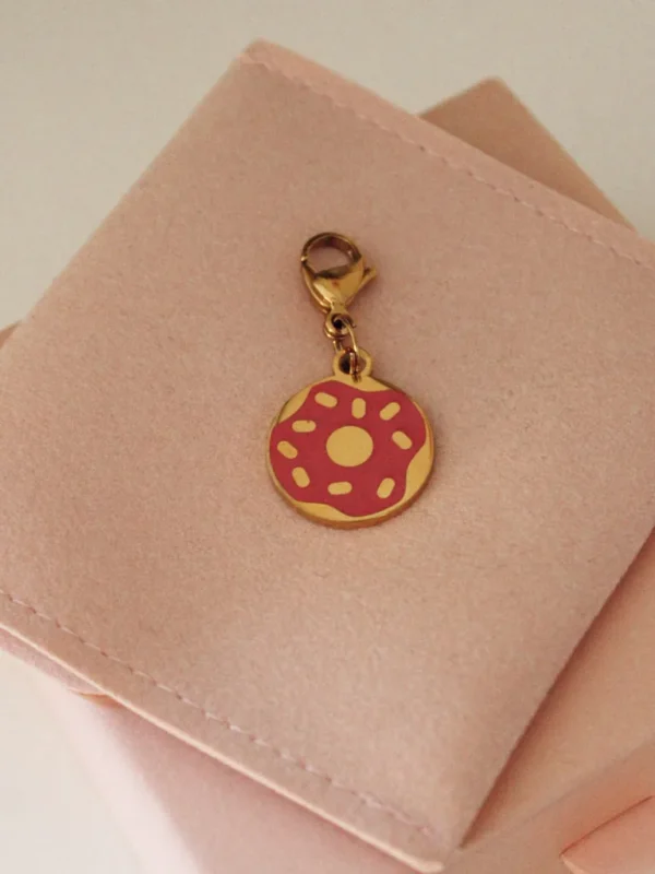Pink-frosted donut charm with sprinkles and a gold-tone clasp on a pale pink pouch