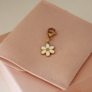Charm de flor margarita blanca con el centro amarillo y mosquetón dorado sobre una funda rosa palo