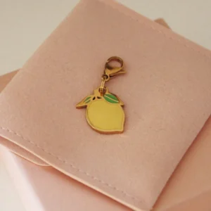 Yellow lemon charm with green leaves and a gold-tone clasp on a pale pink pouch