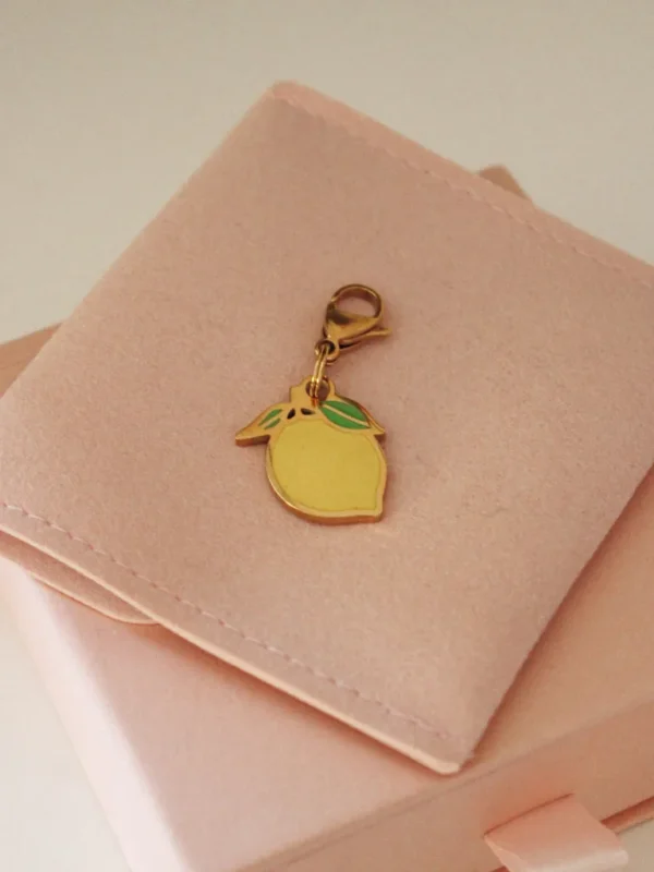 Yellow lemon charm with green leaves and a gold-tone clasp on a pale pink pouch
