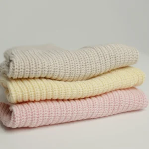 Cream, soft yellow and blush pink cotton knit dog jumpers, folded in a stack