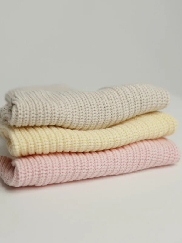 Cream, soft yellow and blush pink cotton knit dog jumpers, folded in a stack