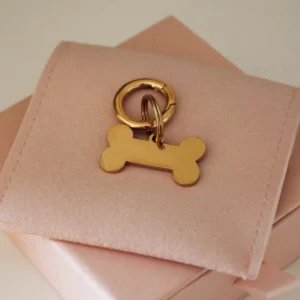 Small gold personalized laser-engraved dog ID tag in a bone shape with a gold-tone ring on a pale pink pouch