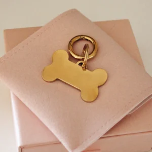 Placa identificativa dorada grande para perro en forma de hueso, personalizada y grabada con láser, con anilla dorada sobre una funda rosa palo