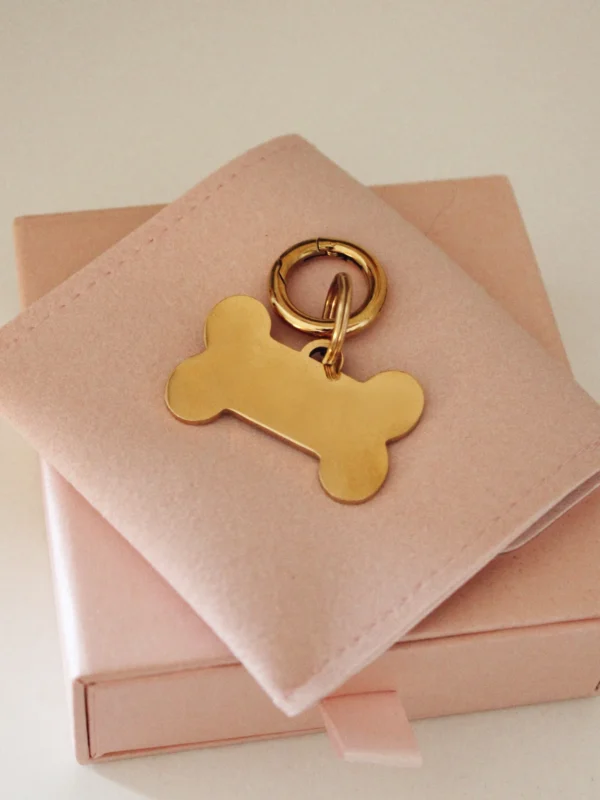 Large gold personalized laser-engraved dog ID tag in a bone shape with a gold-tone ring on a pale pink pouch