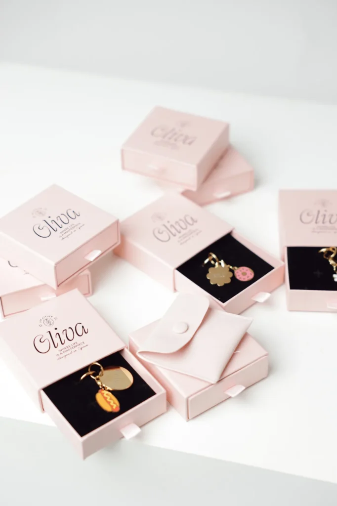 Pale pink Oliva gift boxes holding personalized laser-engraved gold dog ID tags with charms