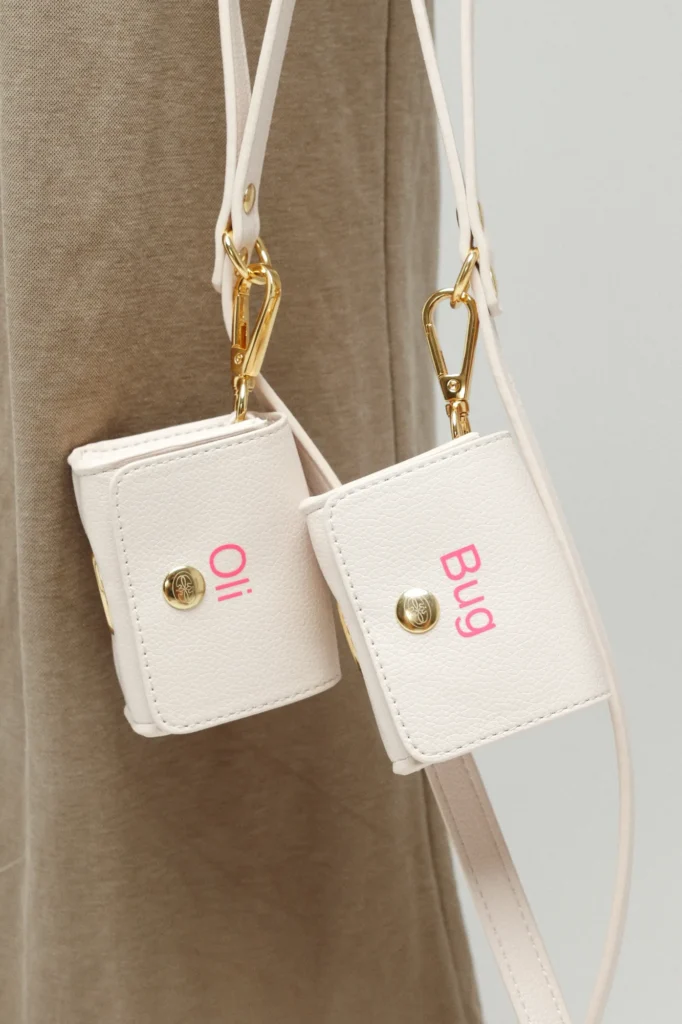Two white poop bag holders personalised in pink with the names Oli and Bug