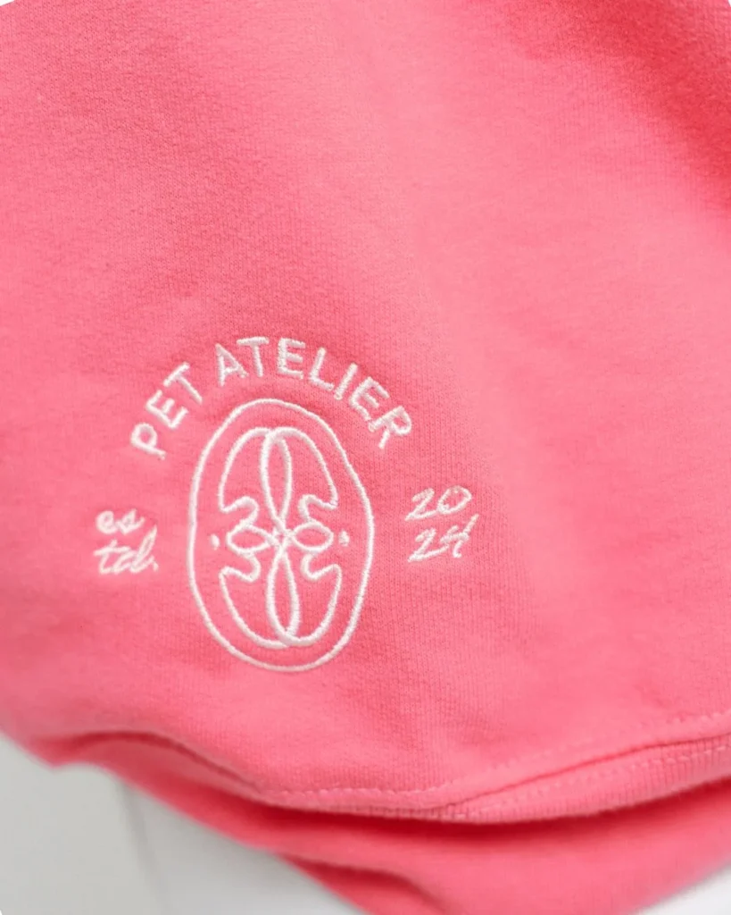 Detalle del emblema de Oliva Pet Atelier bordado en blanco en la sudadera Dog Mom rosa