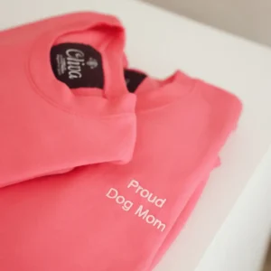 Two folded pink Dog Mom sweatshirts with “Proud Dog Mom” embroidered in white and the Oliva neck label